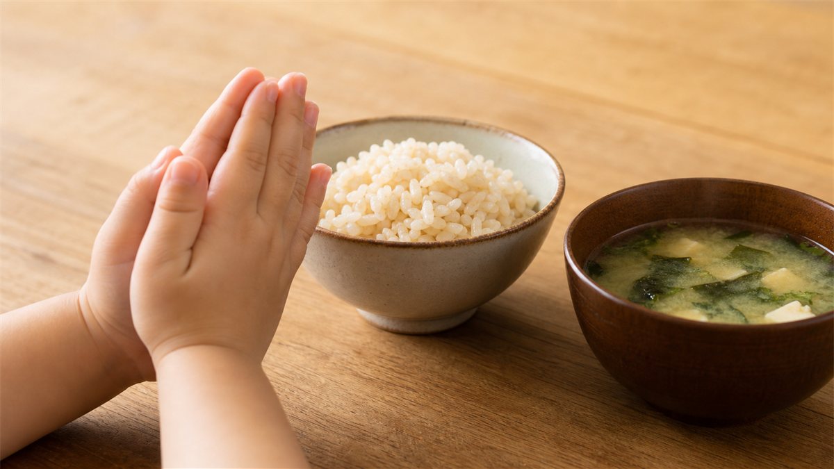 玄米ごはんとみそ汁の素朴な食卓を前に、いただきますと手を合わせる小さな手